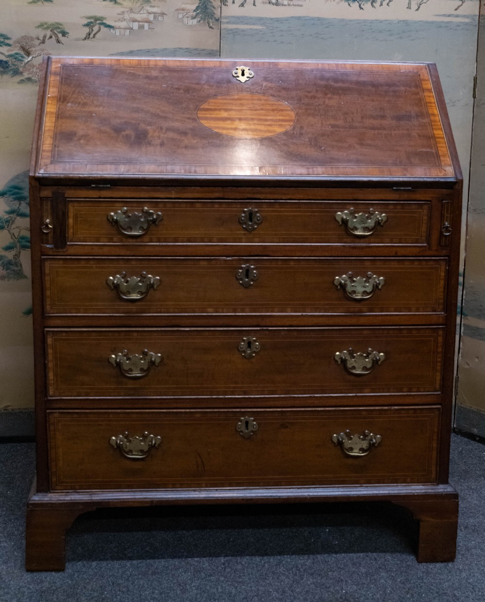 An Edwardian mahogany slant-front bureau featuring satinwood oval inlay, four graduated drawers, and brass handles.