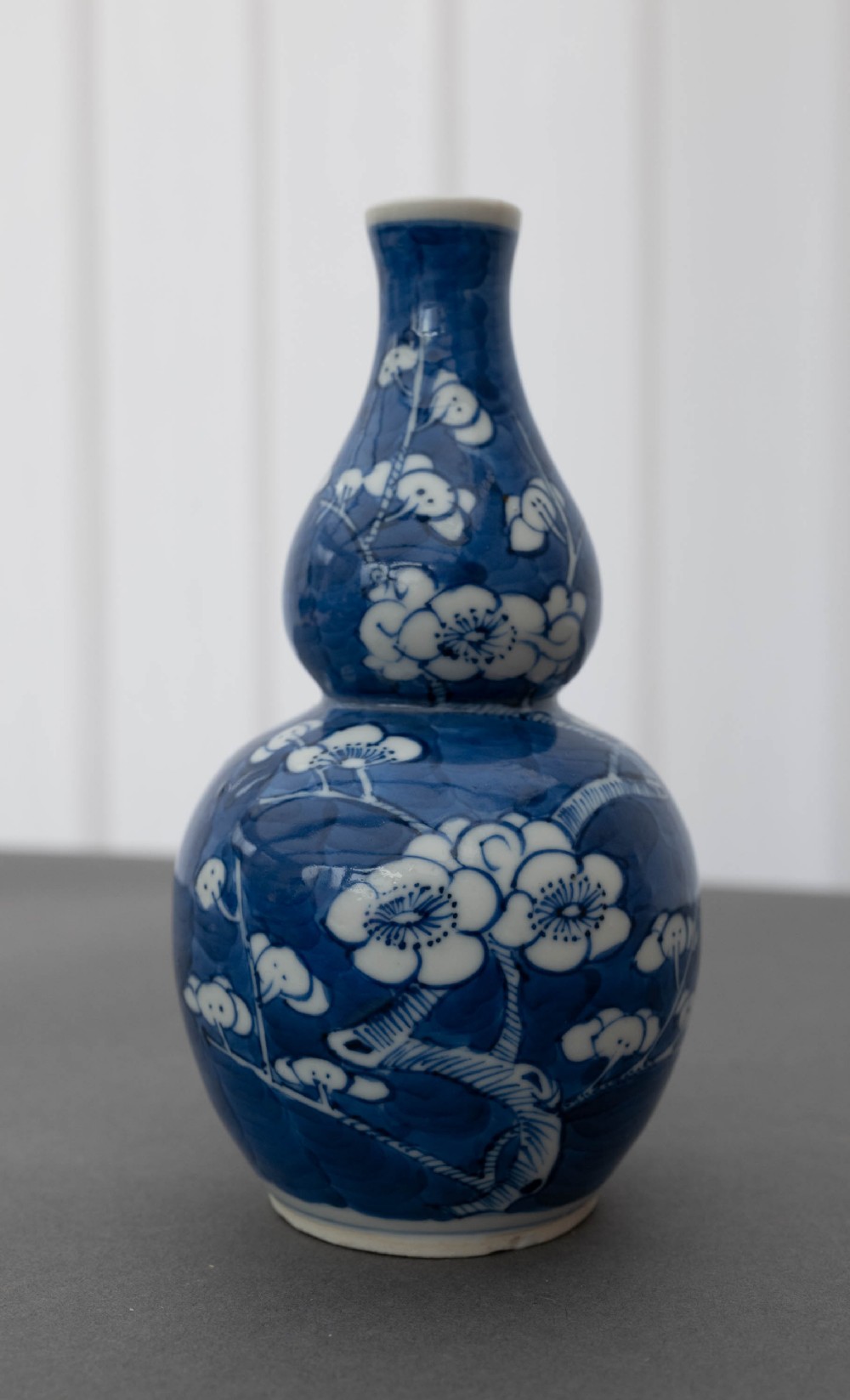 A double gourd-shaped Chinese porcelain vase decorated with white prunus blossom patterns over a dark cobalt blue background.