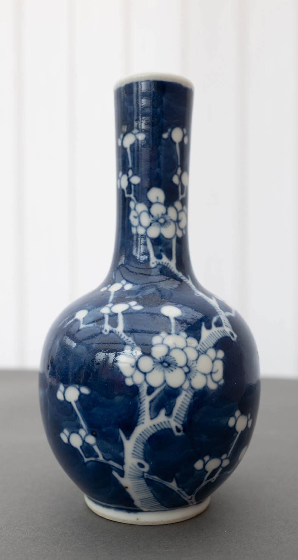 A Chinese porcelain bottle vase featuring a slender neck and globular body decorated with white plum blossom motifs against a cobalt blue background.