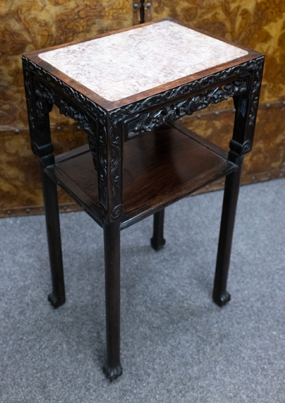 A small rectangular dark padauk wood stand featuring an inset variegated marble top, carved openwork aprons, a lower tier shelf, and straight legs.