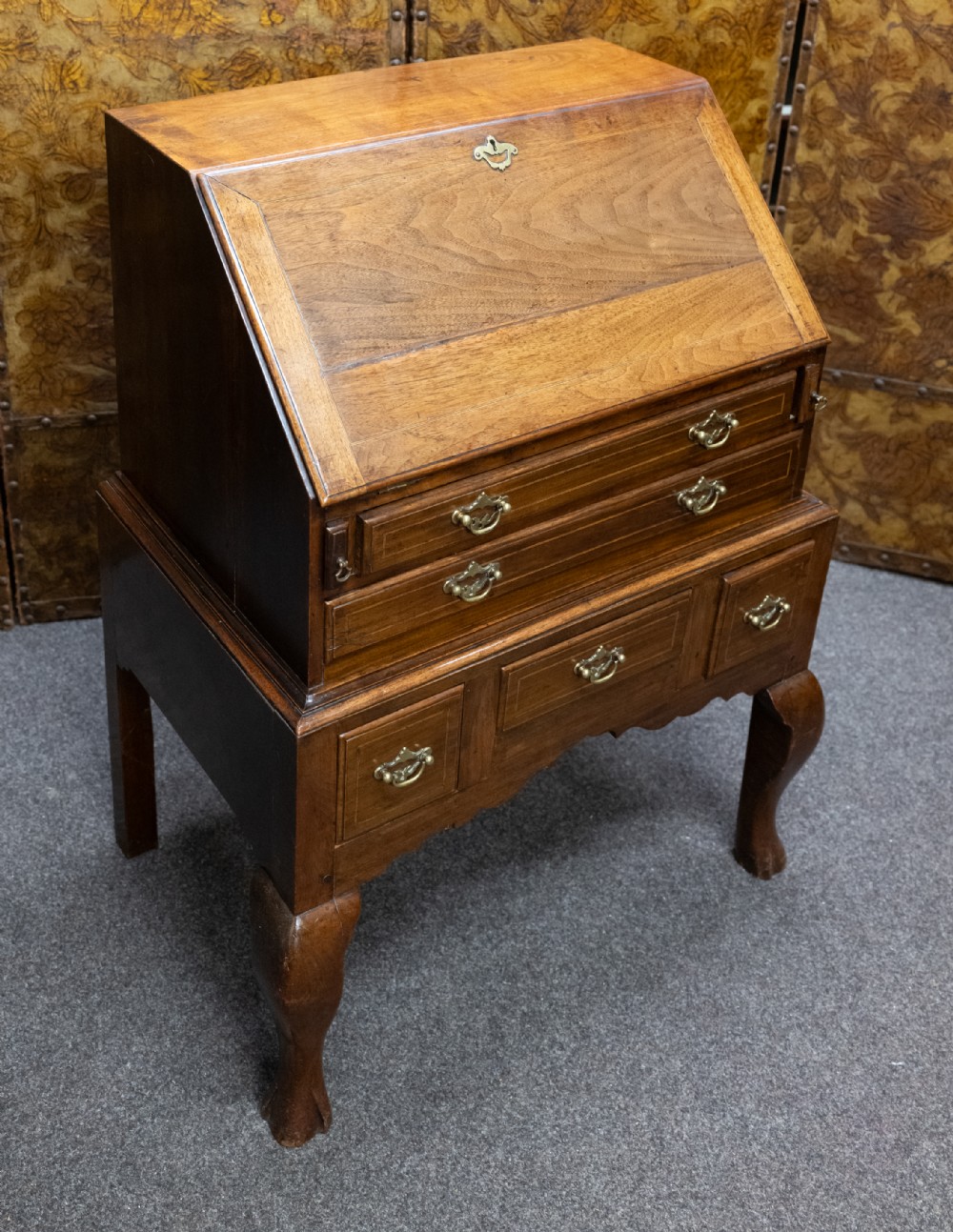 A small solid walnut slant-front bureau featuring a drop-down flap, multiple drawers with brass handles, and cabriole legs.