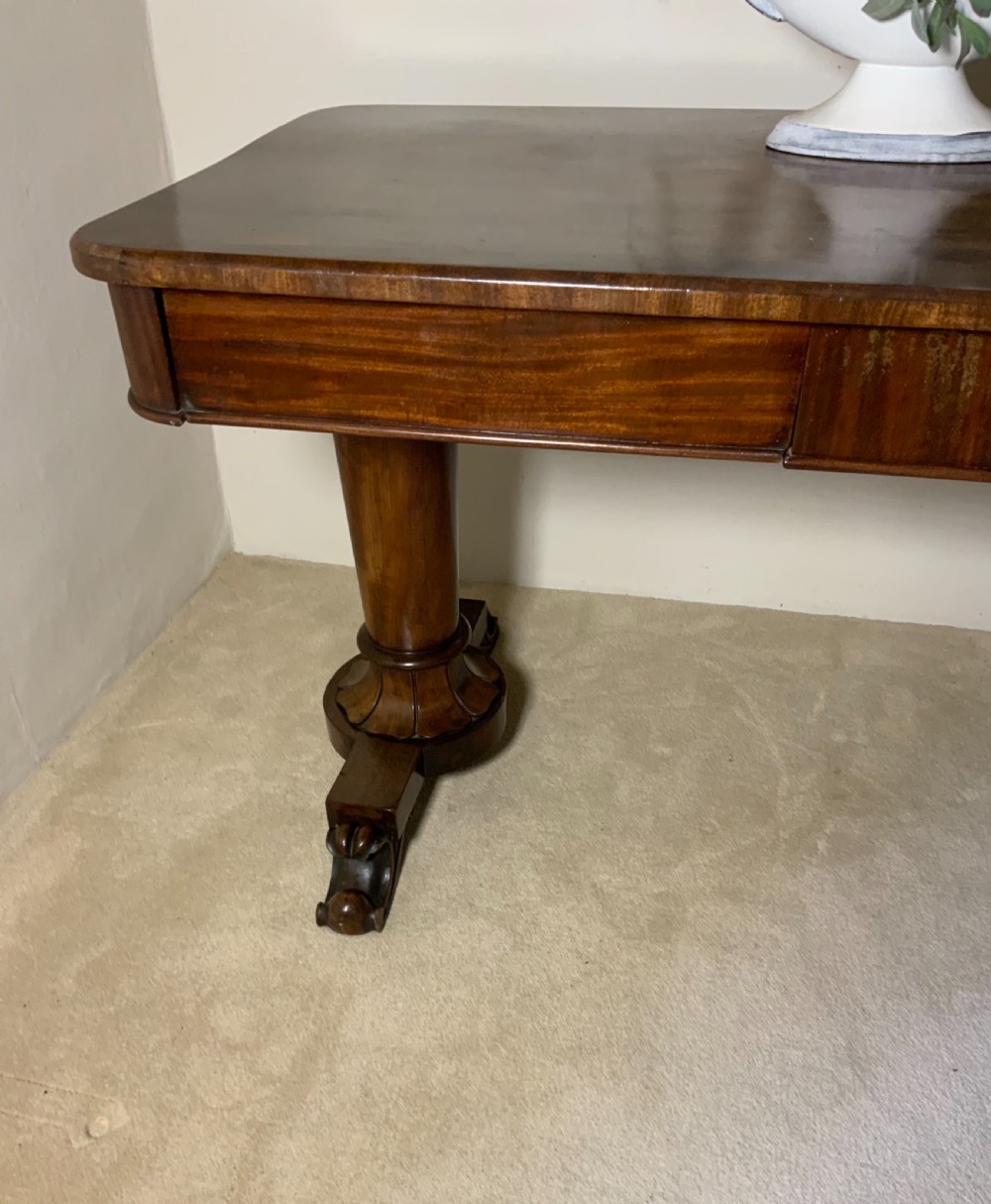 An antique mahogany writing table featuring a rectangular top with rounded corners, a deep frieze, and thick turned legs resting on carved paw feet. View II