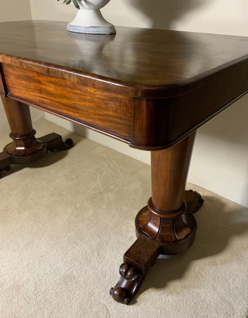 An antique mahogany writing table featuring a rectangular top with rounded corners, a deep frieze, and thick turned legs resting on carved paw feet. View III