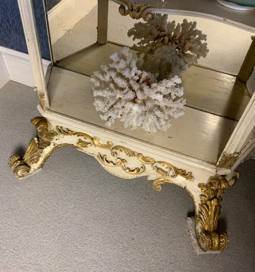 A tall floor-standing cream painted and parcel gilt open display cabinet with four tiers, a mirrored back, and carved Rococo cresting. View II