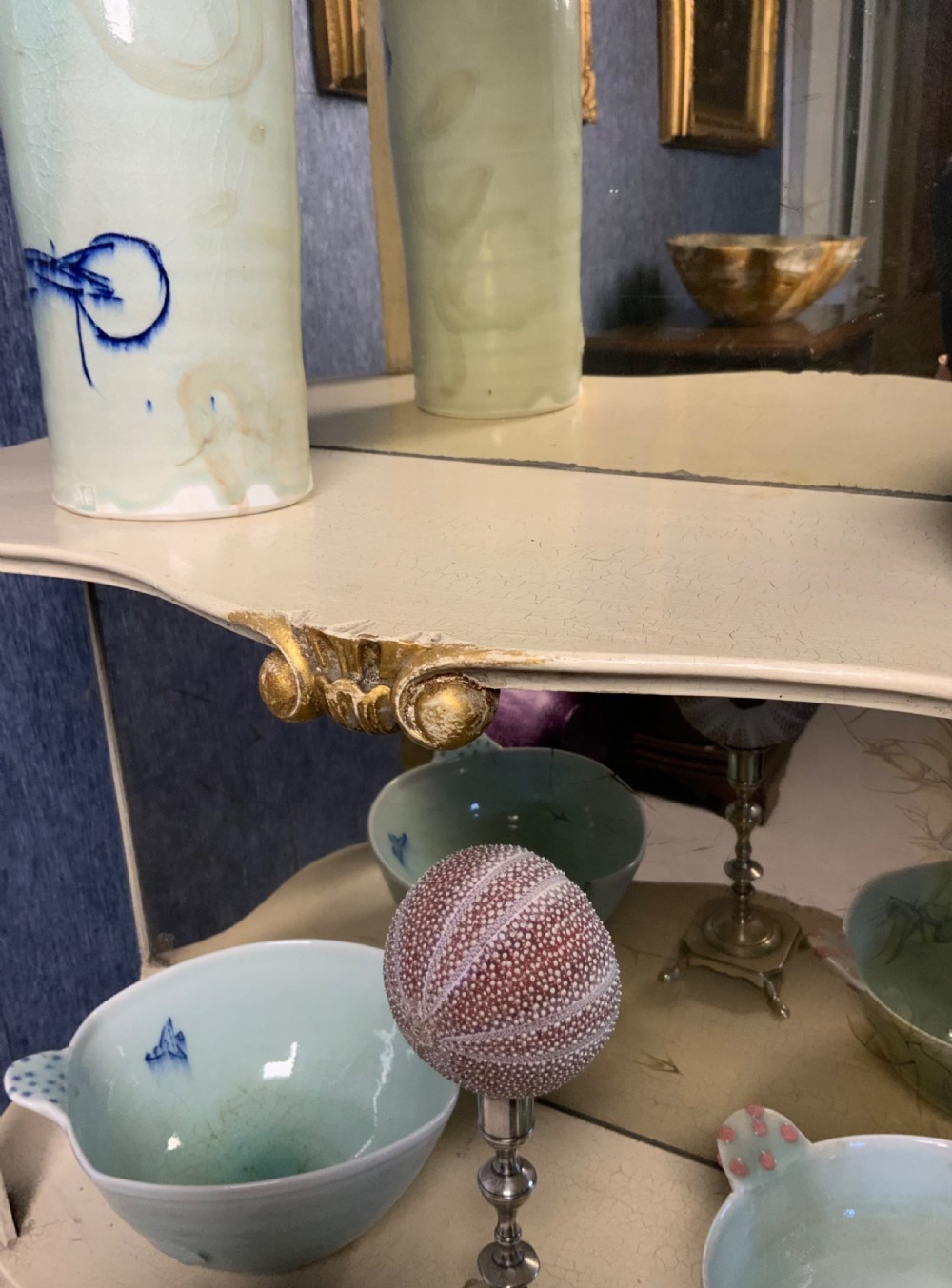 A tall floor-standing cream painted and parcel gilt open display cabinet with four tiers, a mirrored back, and carved Rococo cresting. View VI