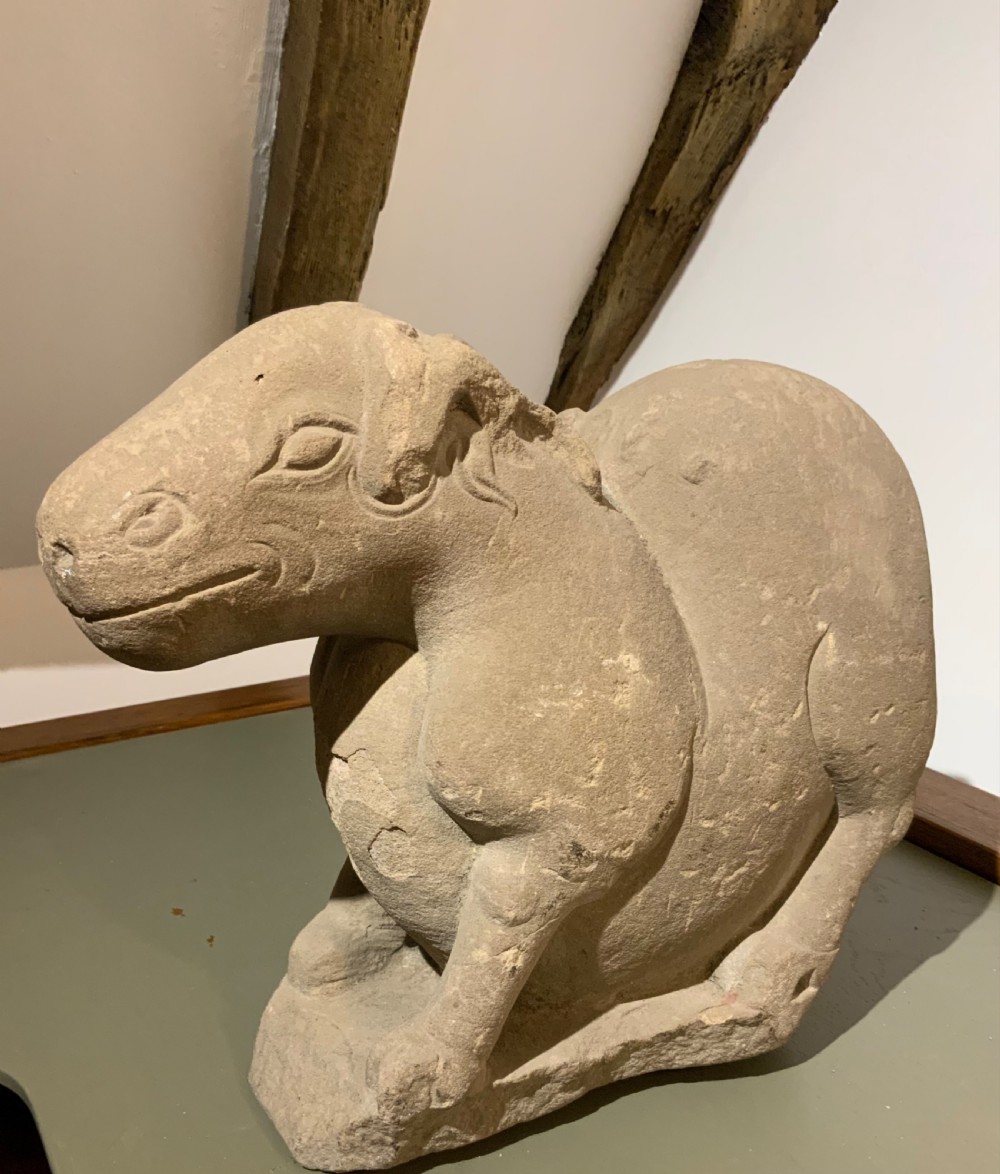 A carved warm grey stone sculpture depicting a resting ram with curled horns, crafted in an ancient Chinese style. View II