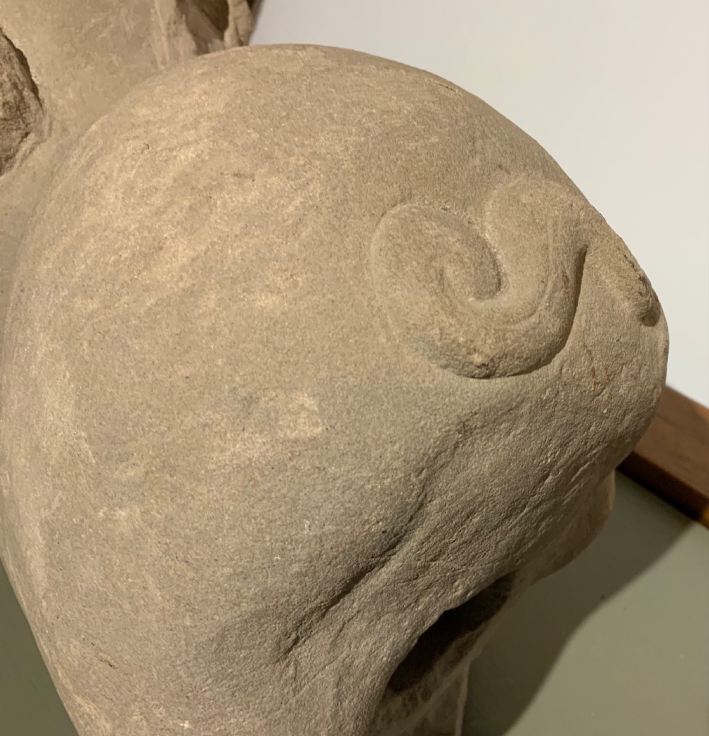 A carved warm grey stone sculpture depicting a resting ram with curled horns, crafted in an ancient Chinese style. View VI
