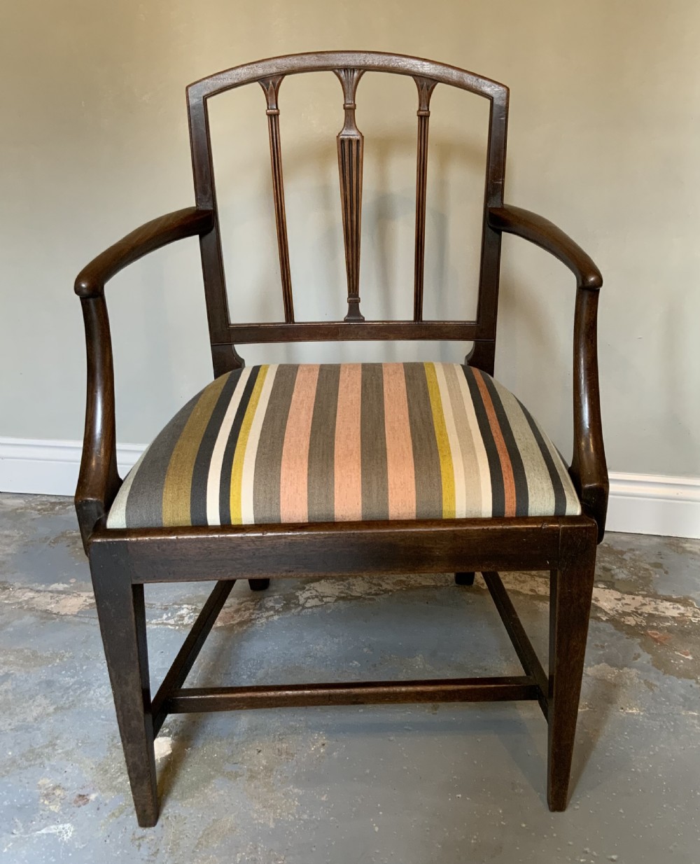 A dark mahogany Georgian open armchair with slender vertical back splats, sweeping armrests, and a multi-coloured striped upholstered seat.