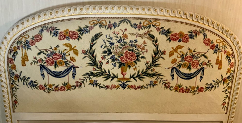 A carved cream painted and parcel gilt five-foot bed frame featuring a arched floral tapestry upholstered headboard and fluted footboard. View II