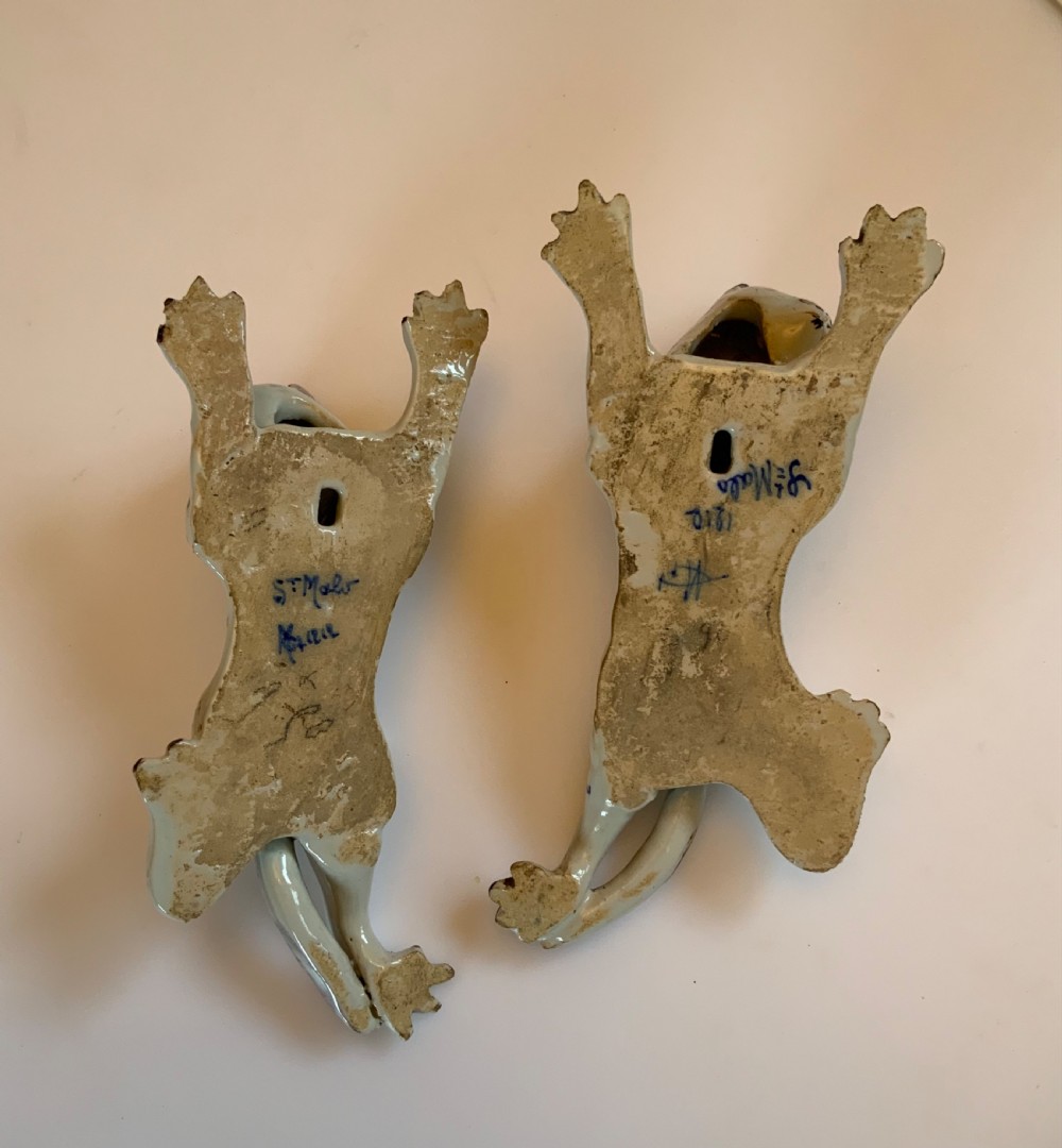 A pair of hand-painted tin-glazed ceramic cat wall pockets styled in recumbent poses with heraldic coat of arms motifs and green glass eyes. View IX