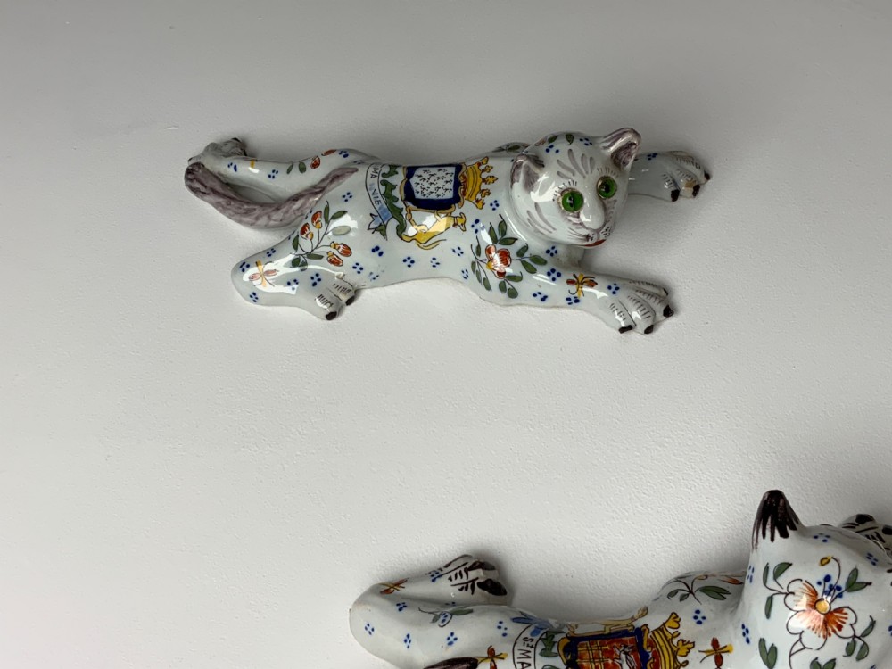A pair of hand-painted tin-glazed ceramic cat wall pockets styled in recumbent poses with heraldic coat of arms motifs and green glass eyes. View X