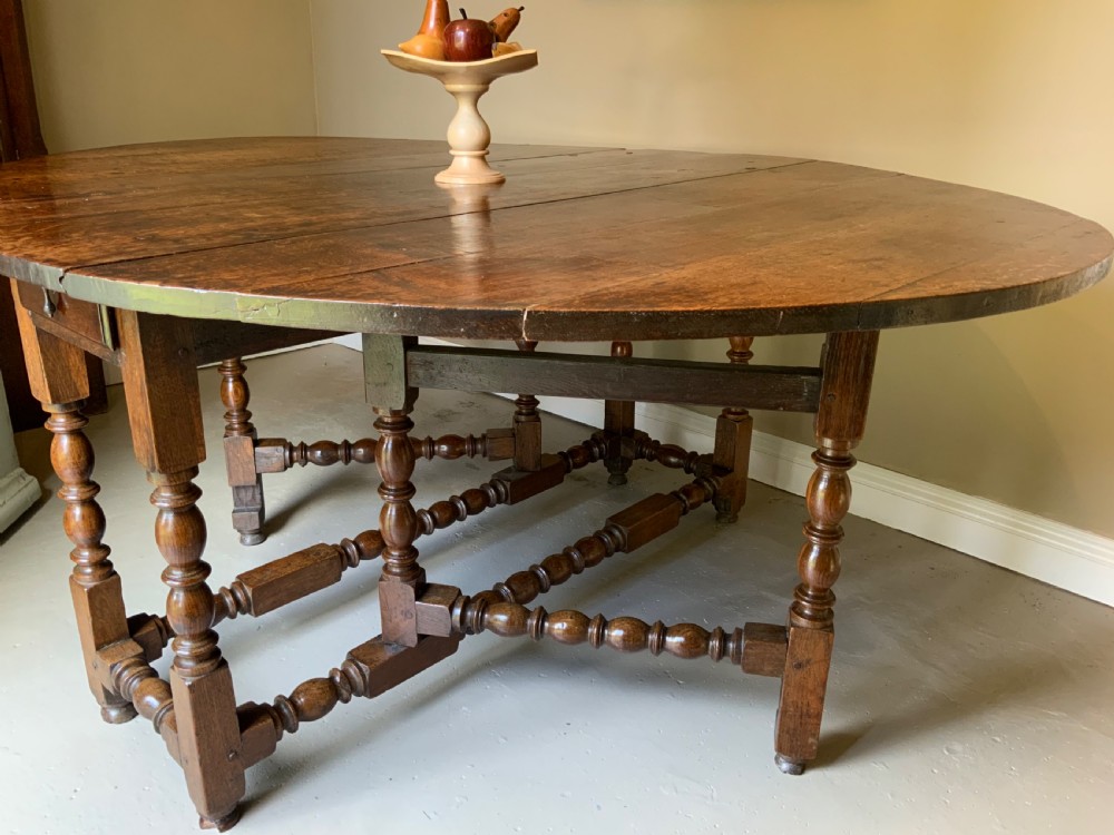 A large 17th-century solid oak gateleg dining table featuring an oval drop-leaf top and turned wooden legs. View VIII