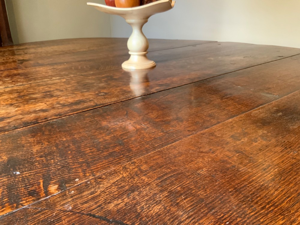 A large 17th-century solid oak gateleg dining table featuring an oval drop-leaf top and turned wooden legs. View V