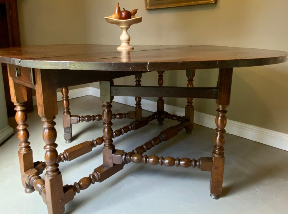 A large 17th-century solid oak gateleg dining table featuring an oval drop-leaf top and turned wooden legs. View VII