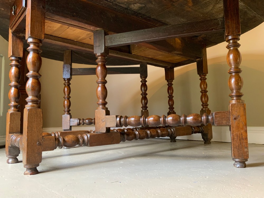 A large 17th-century solid oak gateleg dining table featuring an oval drop-leaf top and turned wooden legs. View IX
