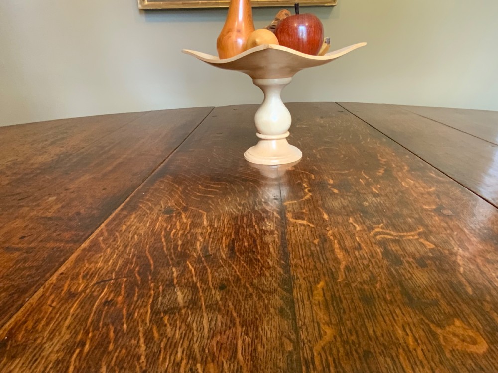 A large 17th-century solid oak gateleg dining table featuring an oval drop-leaf top and turned wooden legs. View X
