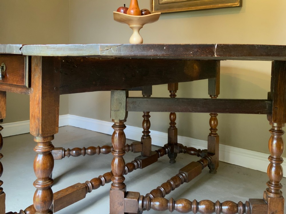 A large 17th-century solid oak gateleg dining table featuring an oval drop-leaf top and turned wooden legs. View XI