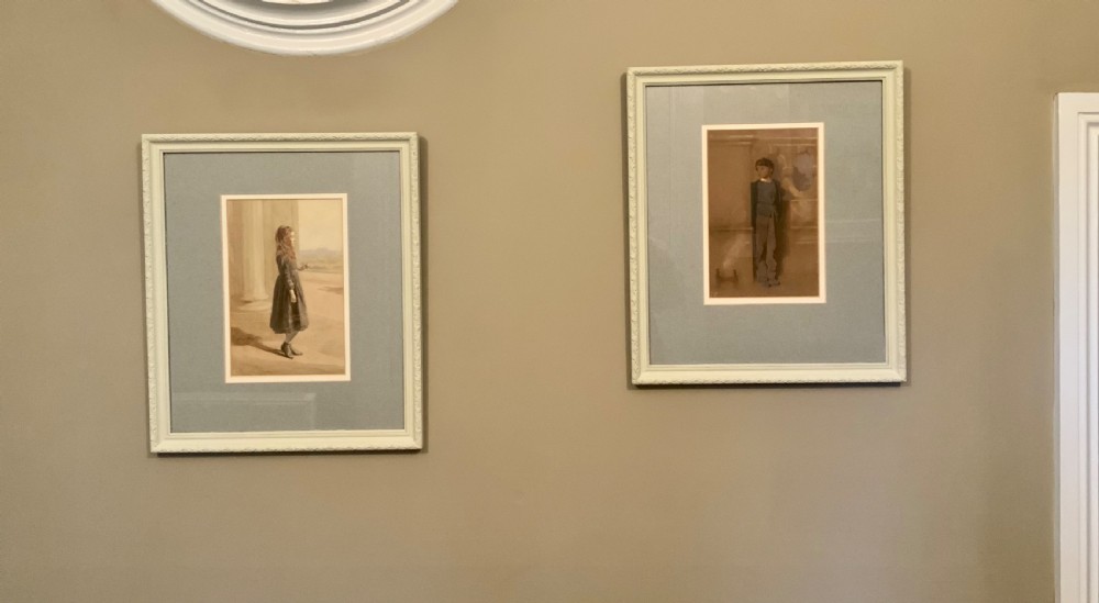 A pair of framed Victorian watercolour portraits depicting a young girl and a young boy set within pale blue mounts and off-white frames.