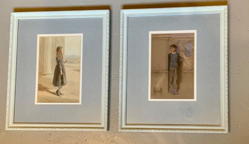 A pair of framed Victorian watercolour portraits depicting a young girl and a young boy set within pale blue mounts and off-white frames. View V