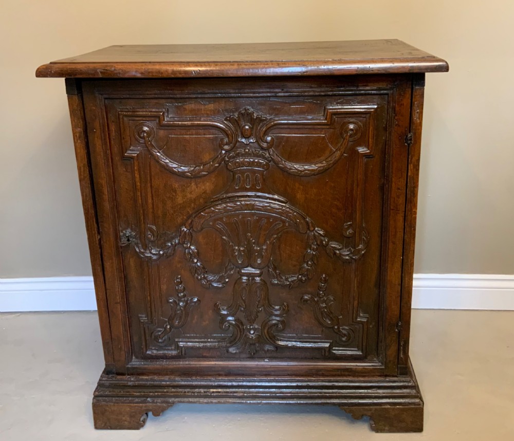 An Italian walnut Baroque cabinet featuring a single door decorated with relief carvings of an urn and floral garlands on a moulded plinth base.