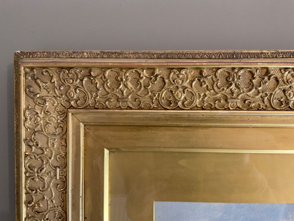 A framed 19th-century watercolour painting depicting a river running through a green landscape with trees and distant hills, set within an ornate gold gilt frame. View II