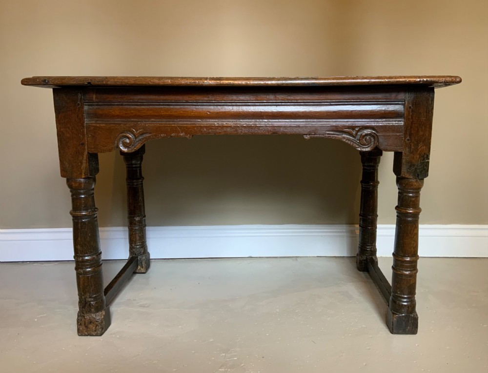 A 17th-century dark oak side table featuring turned legs, carved scroll spandrels, and lower stretcher rails.