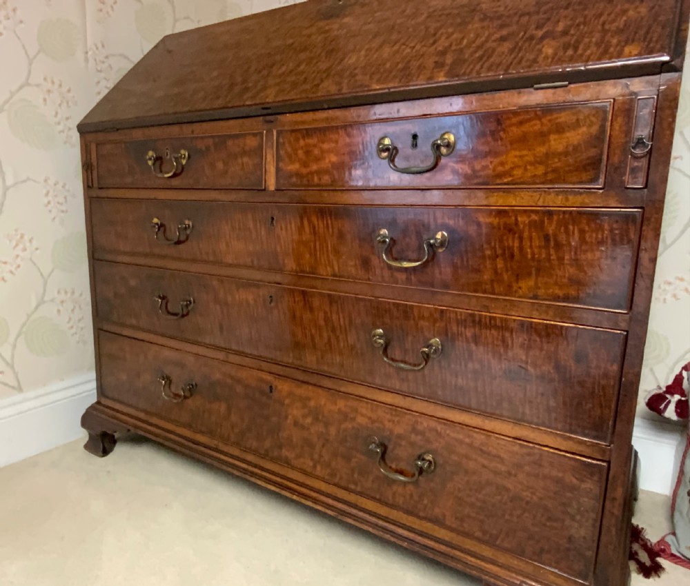 A George III mahogany bureau featuring a sloping front flap over four graduated drawers with brass swan-neck handles and bracket feet. View II