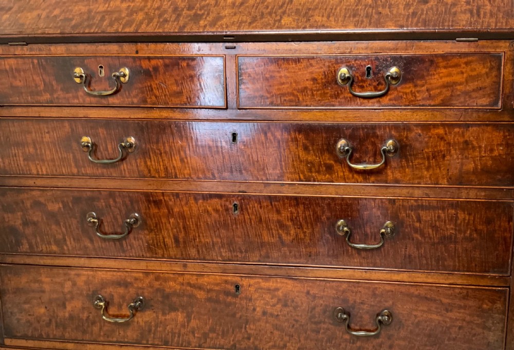 A George III mahogany bureau featuring a sloping front flap over four graduated drawers with brass swan-neck handles and bracket feet. View IV