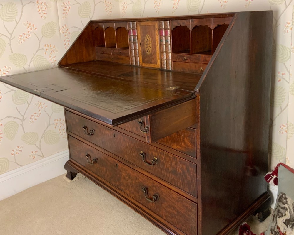 A George III mahogany bureau featuring a sloping front flap over four graduated drawers with brass swan-neck handles and bracket feet. View XII