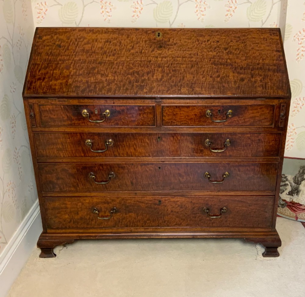 A George III mahogany bureau featuring a sloping front flap over four graduated drawers with brass swan-neck handles and bracket feet.