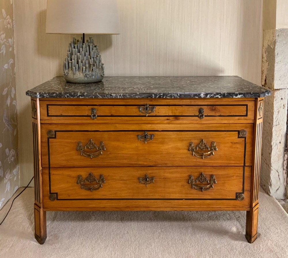 A late 18th-century French Louis XVI style walnut commode featuring three drawers, geometric ebonised inlay, brass hardware, and a dark grey marble top. View II