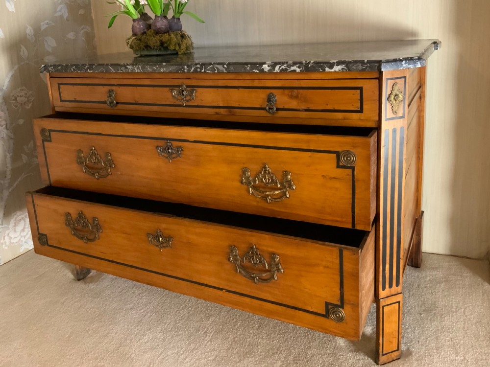 A late 18th-century French Louis XVI style walnut commode featuring three drawers, geometric ebonised inlay, brass hardware, and a dark grey marble top. View III