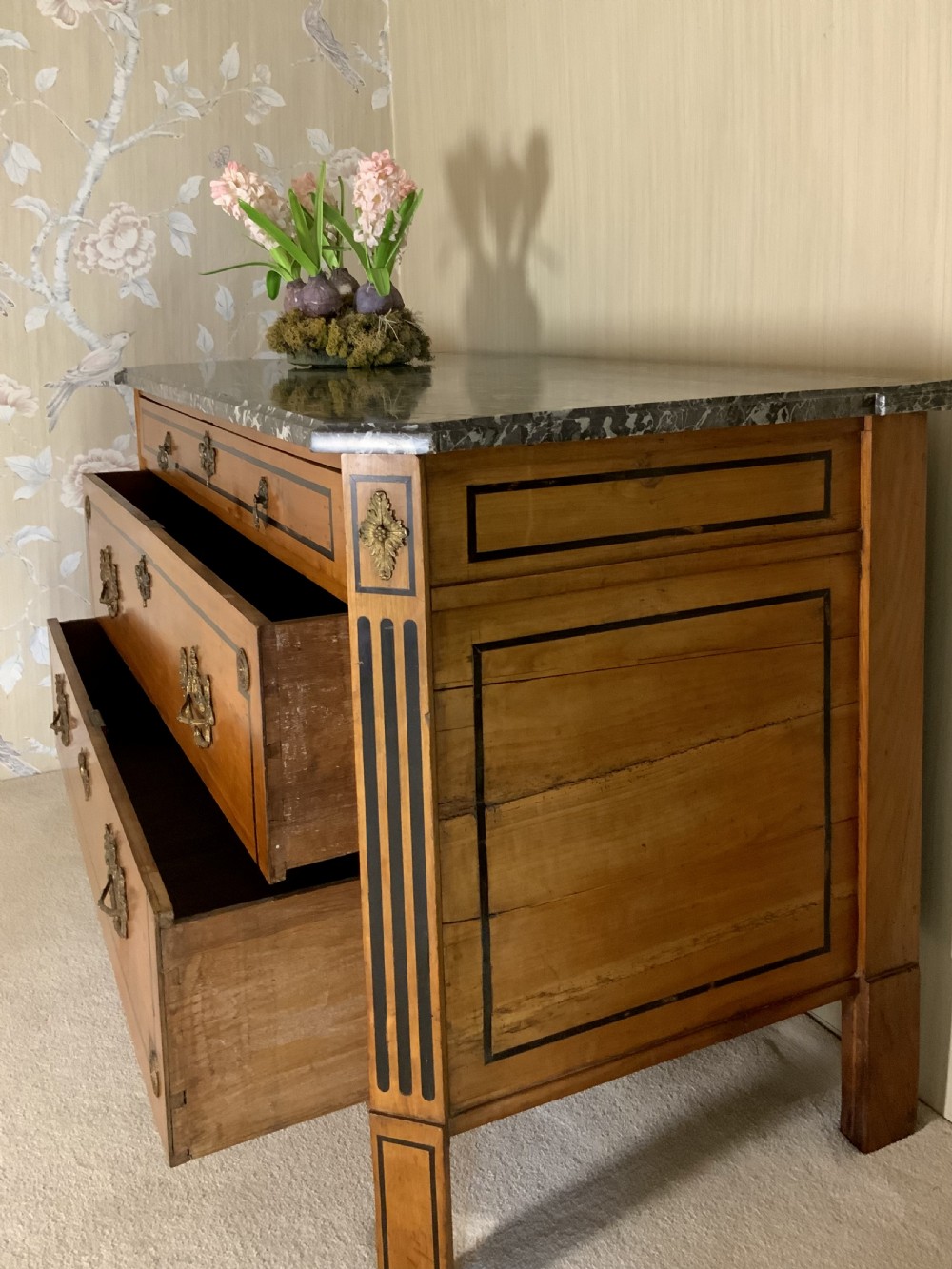 A late 18th-century French Louis XVI style walnut commode featuring three drawers, geometric ebonised inlay, brass hardware, and a dark grey marble top. View XII