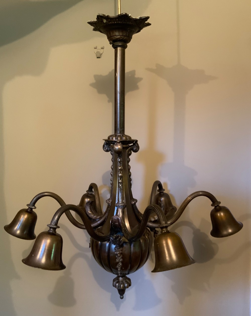 A dark patinated bronze five-arm chandelier featuring downward-facing bell shades, reeded scroll arms, and an ornate central stem.