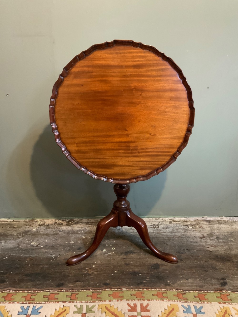 An antique Georgian mahogany tilt-top tripod table with a scalloped piecrust rim, turned central pedestal, and three cabriole legs.