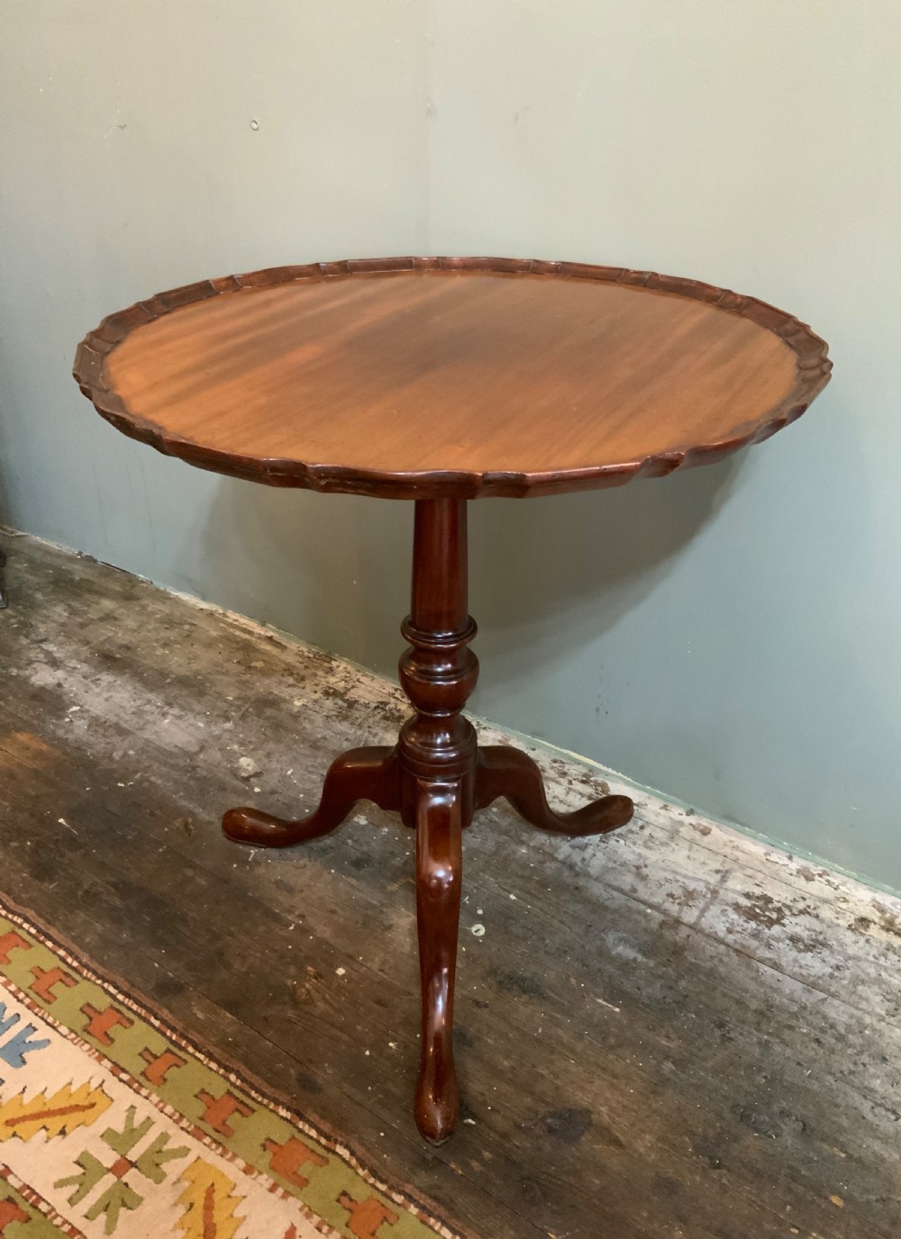 An antique Georgian mahogany tilt-top tripod table with a scalloped piecrust rim, turned central pedestal, and three cabriole legs. View II