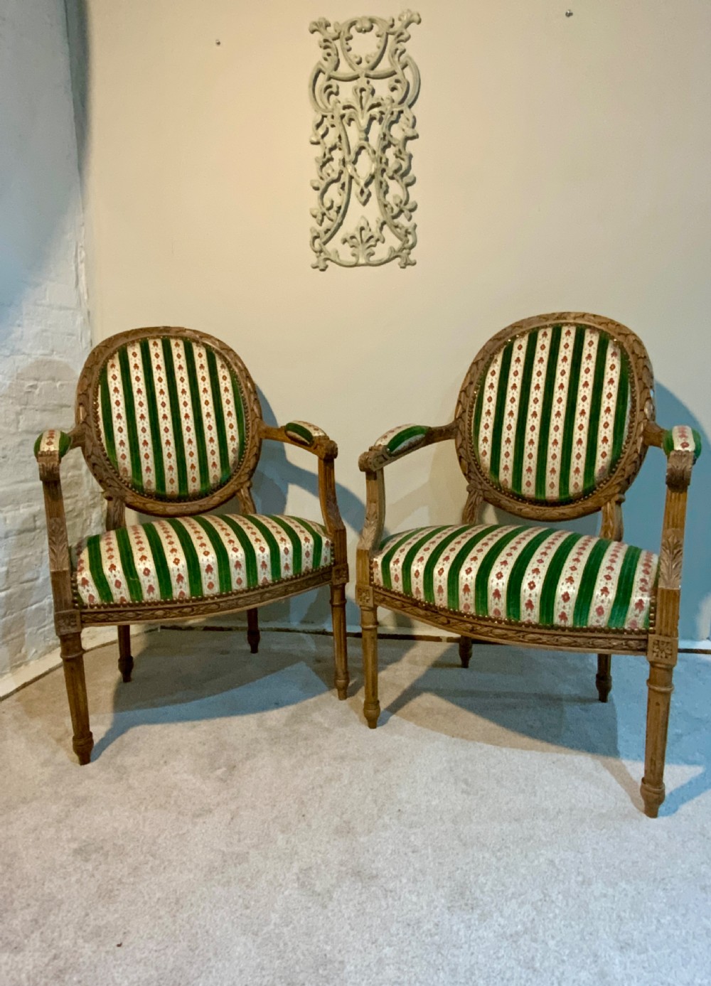 A pair of 19th-century French armchairs featuring carved wooden frames, oval backrests, and green and cream striped fabric upholstery.
