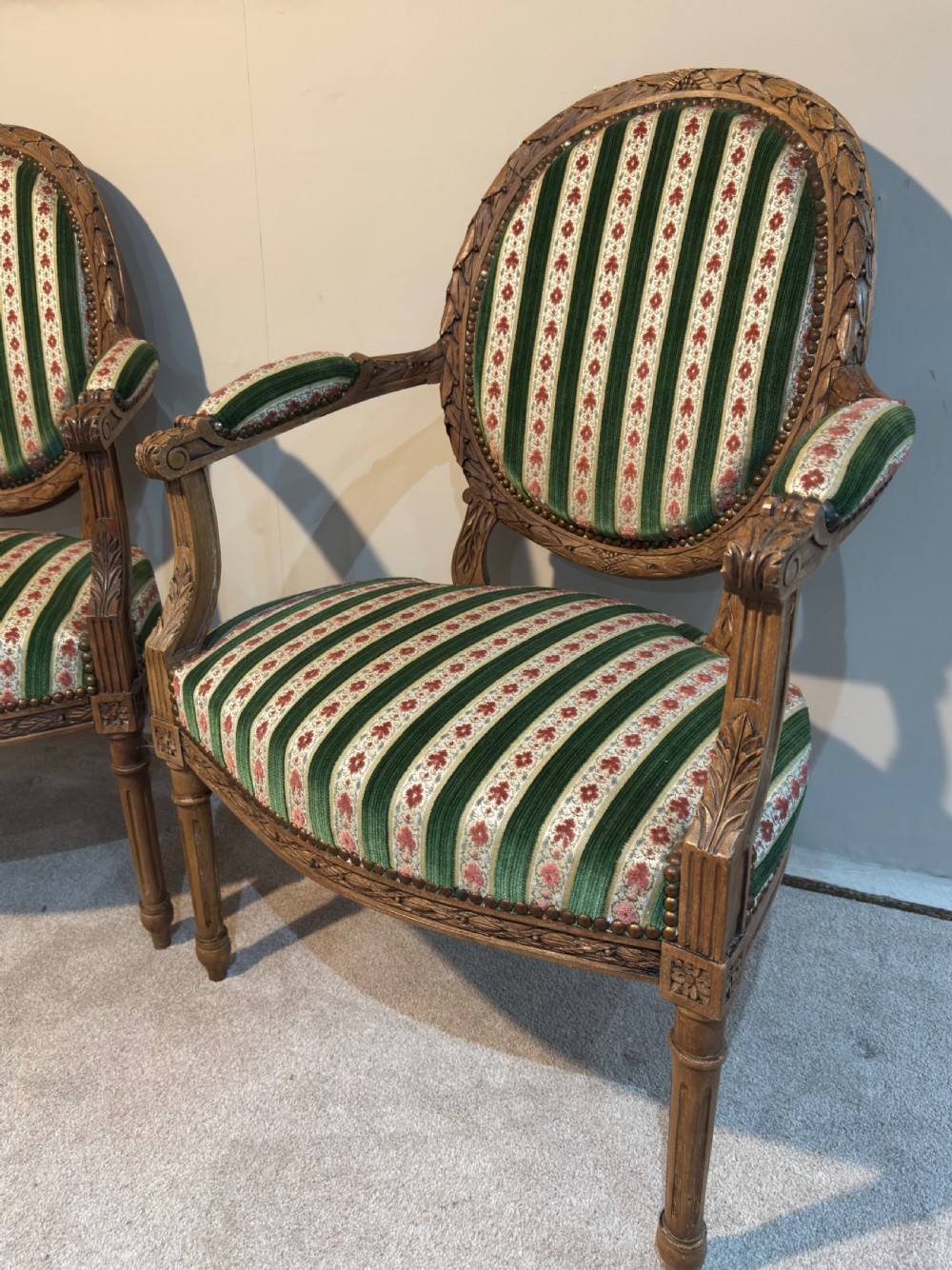 A pair of 19th-century French armchairs featuring carved wooden frames, oval backrests, and green and cream striped fabric upholstery. View II