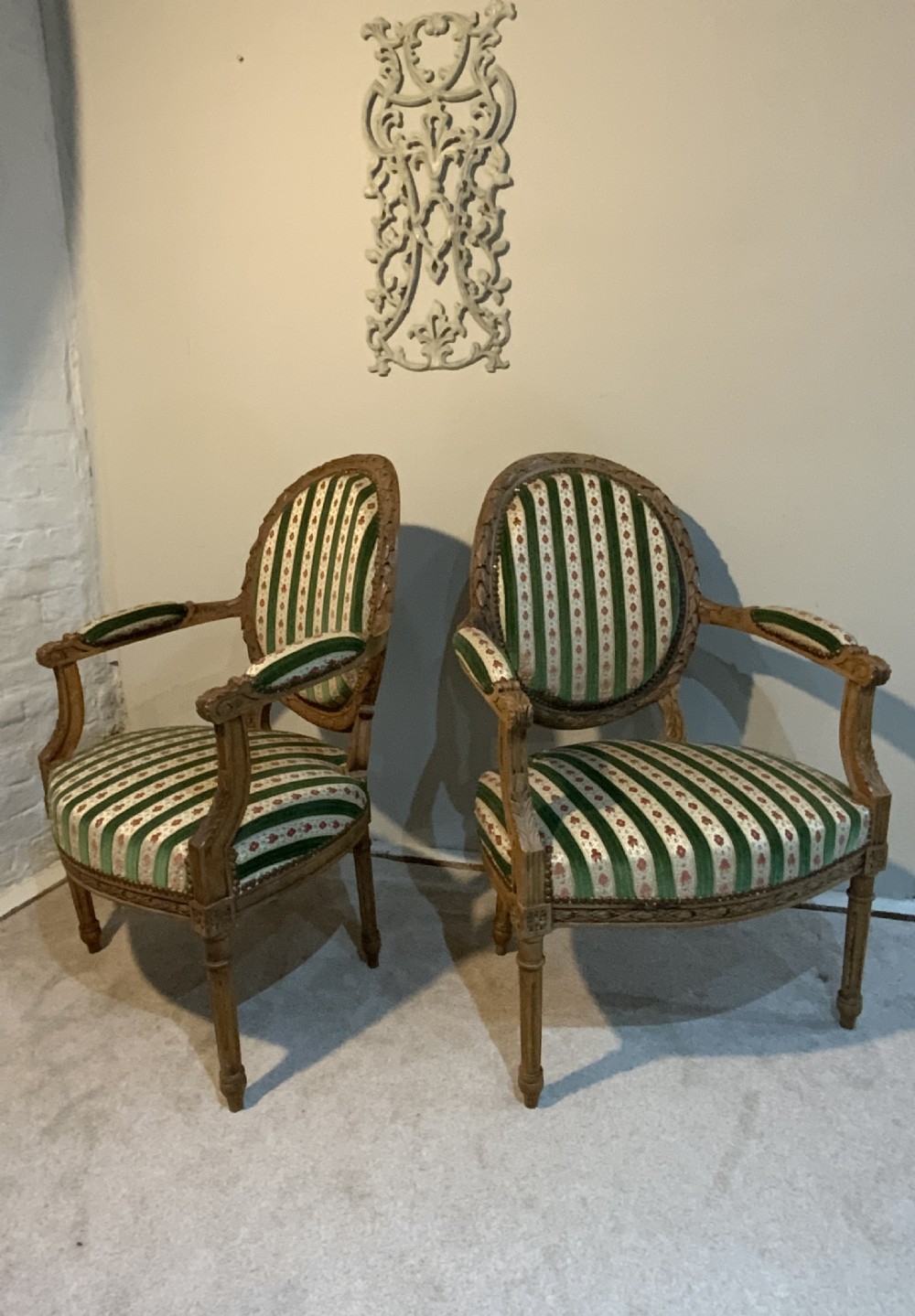 A pair of 19th-century French armchairs featuring carved wooden frames, oval backrests, and green and cream striped fabric upholstery. View VI