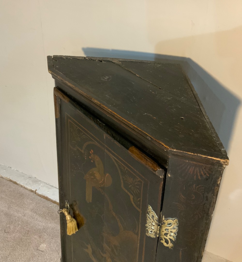 An 18th-century black lacquered corner cabinet featuring gilt chinoiserie artwork of figures, architecture, and a parrot, fitted with decorative brass hinges. View V