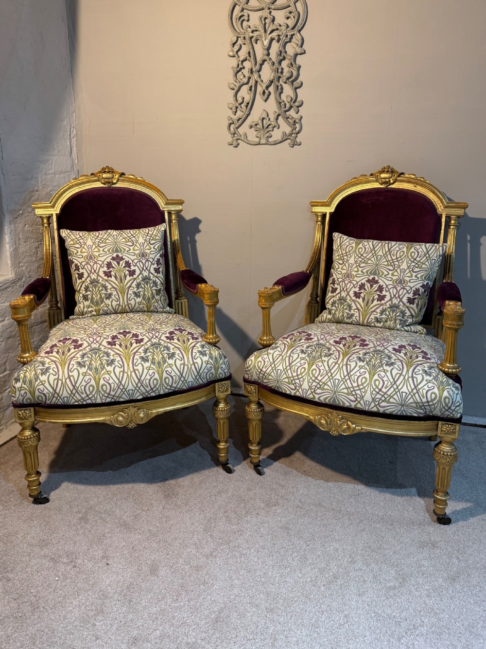 A pair of giltwood armchairs featuring carved frames, fluted legs, purple velvet backrests, and botanical patterned fabric upholstery.