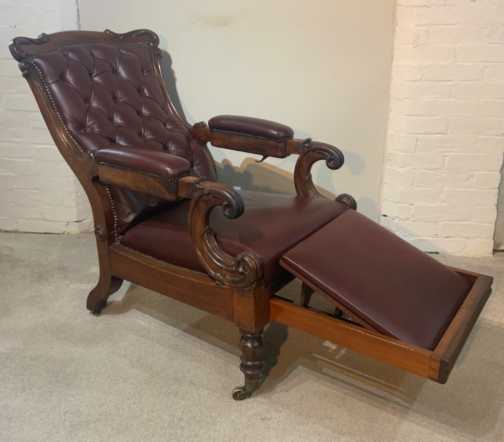 A William IV mahogany library armchair upholstered in button-back burgundy leather with an extending footrest and carved scroll arms.