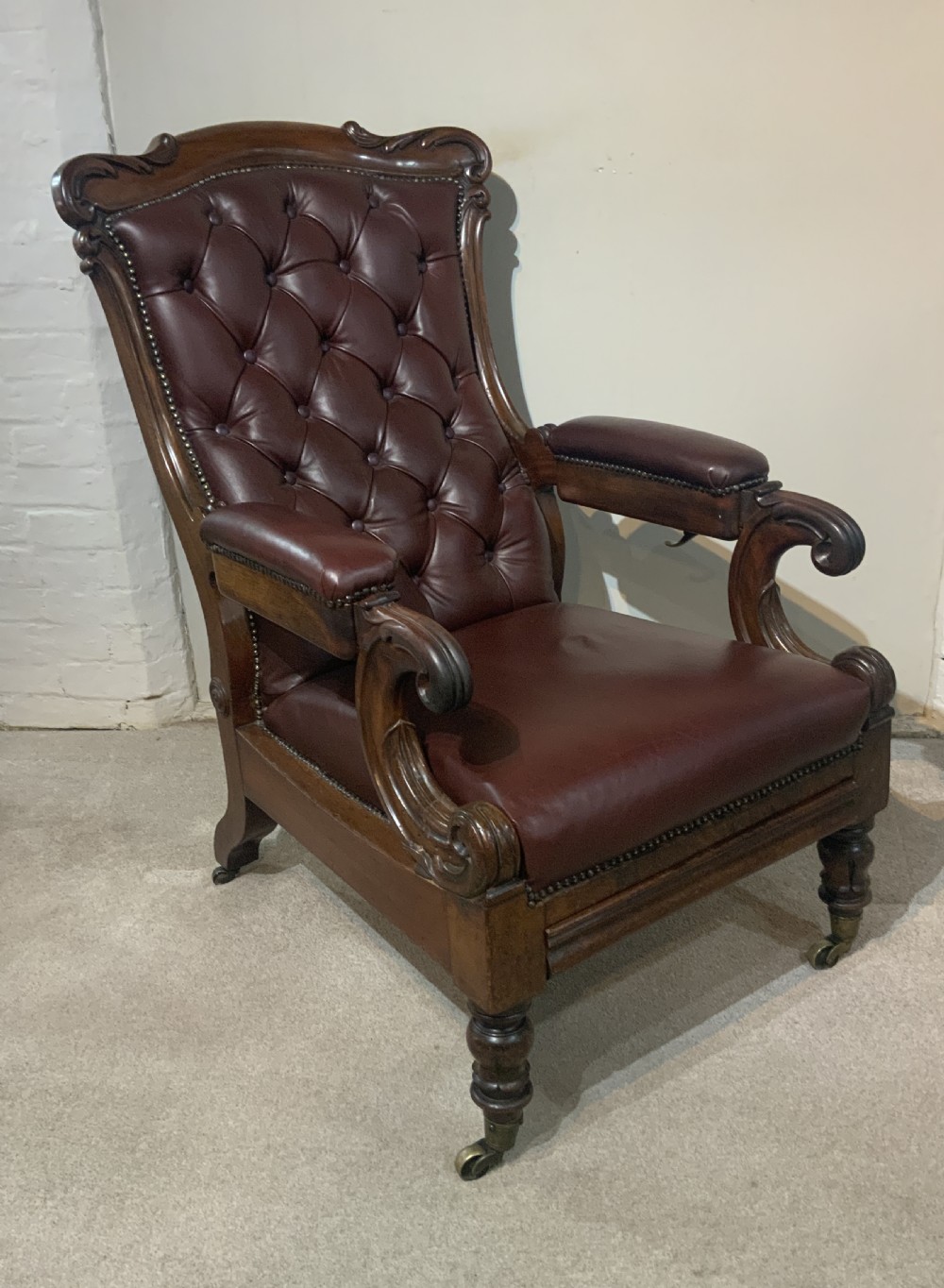 A William IV mahogany library armchair upholstered in button-back burgundy leather with an extending footrest and carved scroll arms. View III