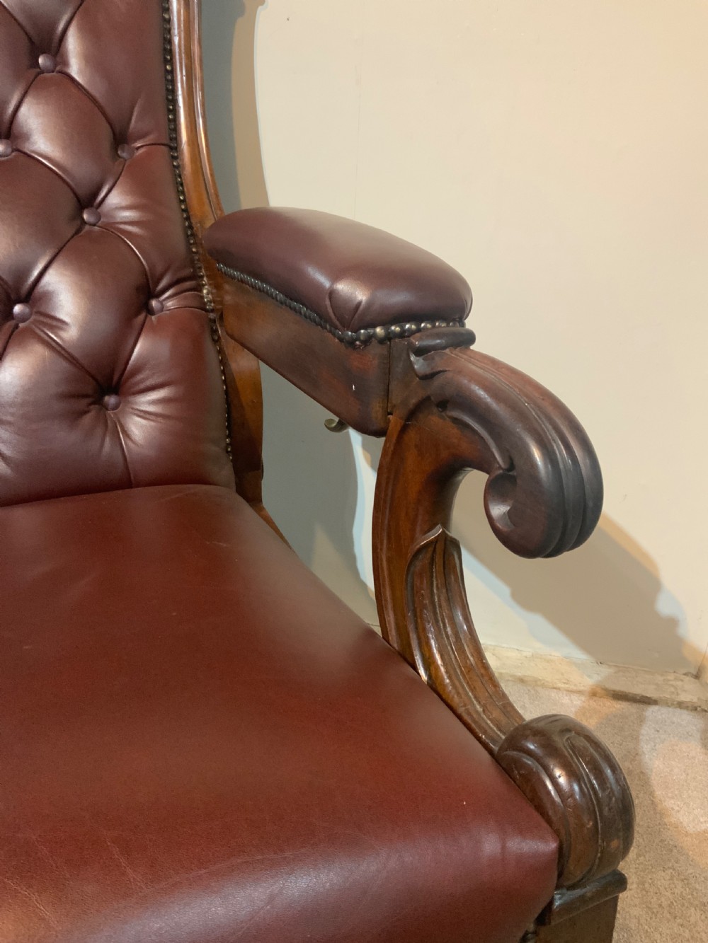 A William IV mahogany library armchair upholstered in button-back burgundy leather with an extending footrest and carved scroll arms. View VI