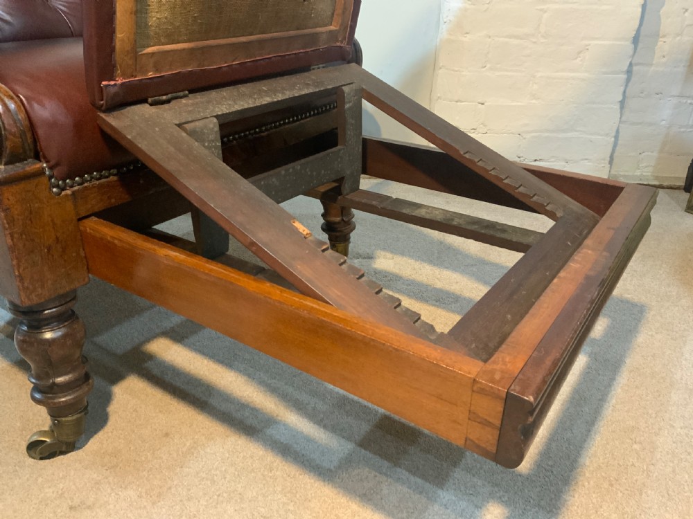 A William IV mahogany library armchair upholstered in button-back burgundy leather with an extending footrest and carved scroll arms. View VII