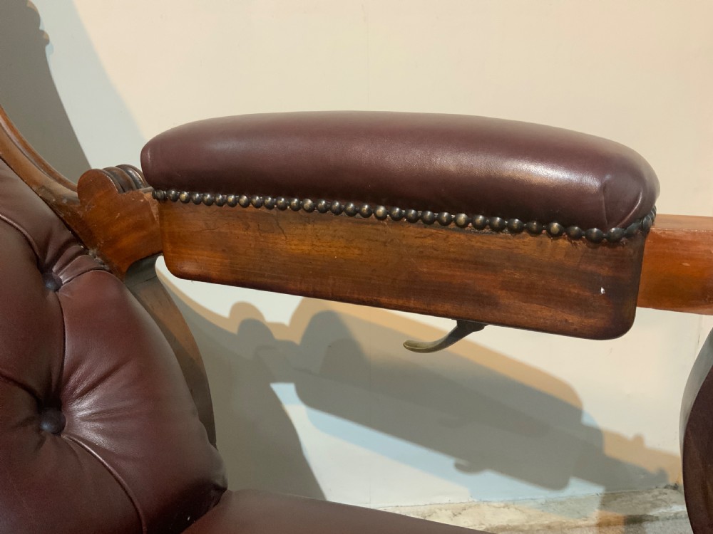 A William IV mahogany library armchair upholstered in button-back burgundy leather with an extending footrest and carved scroll arms. View VIII