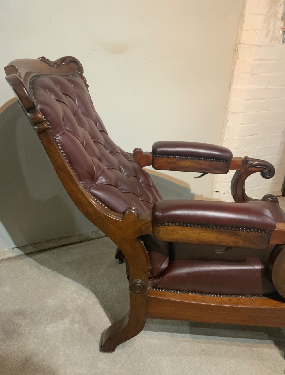 A William IV mahogany library armchair upholstered in button-back burgundy leather with an extending footrest and carved scroll arms. View IX