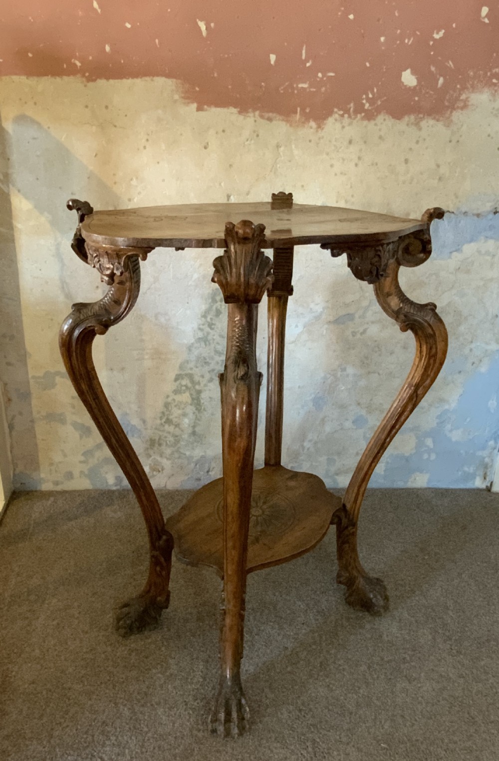 A carved Italian walnut three-legged occasional table featuring sculptural legs shaped like mythical figures terminating in claw feet with a lower undertier shelf.