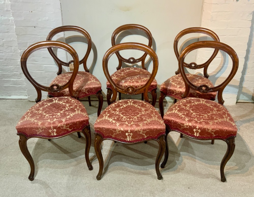 A set of six early Victorian rosewood balloon-back dining chairs with red damask upholstery and cabriole legs.