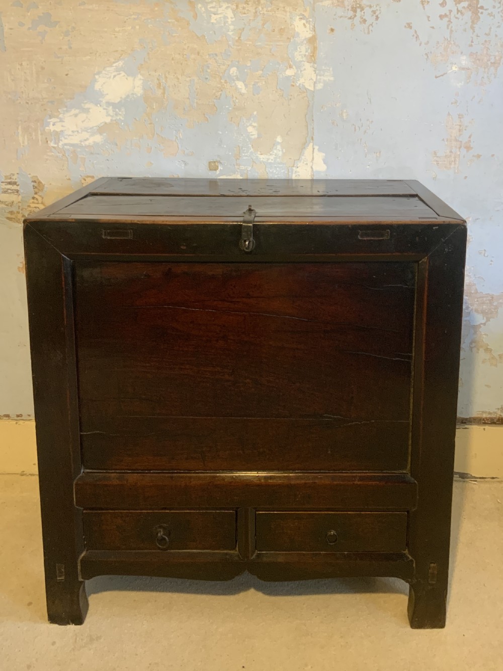 A dark brown 18th-century Chinese wooden chest featuring a top-opening lid, two lower drawers with metal ring handles, and iron latch hardware.